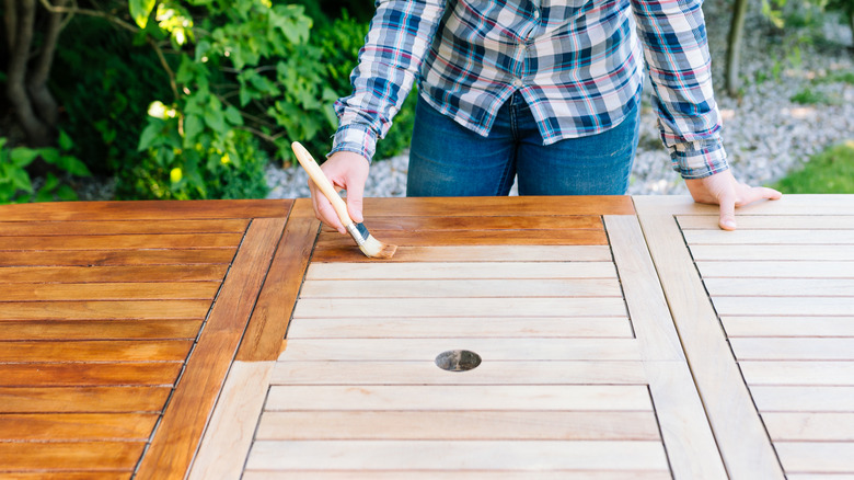 woman staining outdoor wooden table