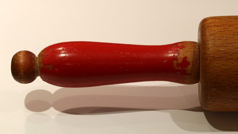 Close up image of an antique rolling pin with a handle painted red