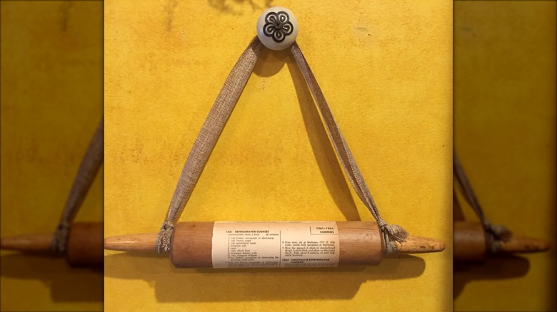 Rolling pin hung on yellow painted wall with recipe attached to it