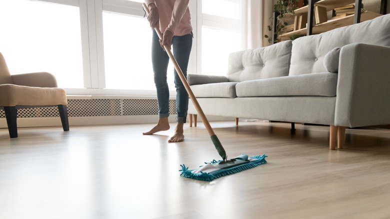 person mopping laminate floors in living room with couch