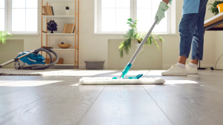 A woman cleaning a laminate floor with a dry mop