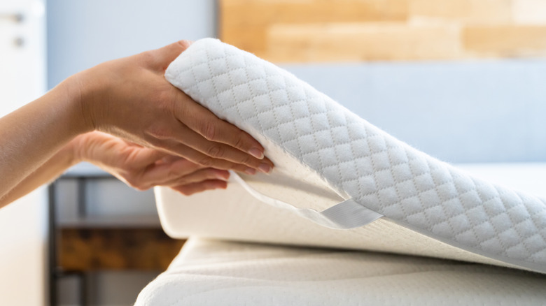 Hands holding a white mattress topper and placing it on a mattress