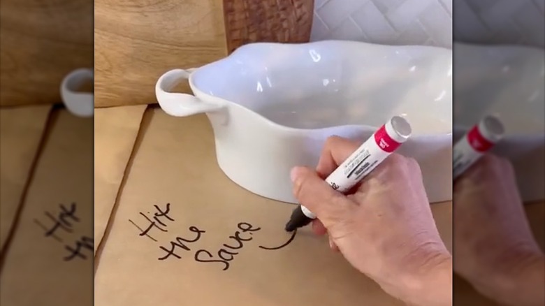 Person writing on kraft paper, labeling bowl on kitchen countertop