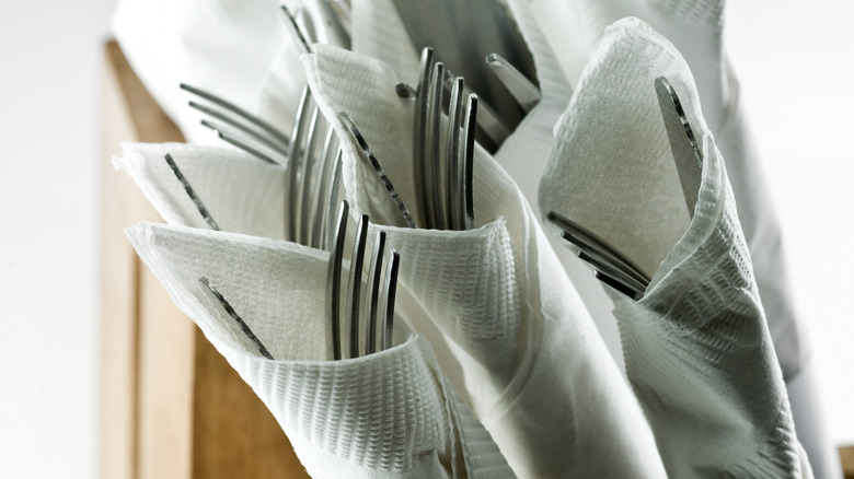 Rolled bunches of silverware in white napkins