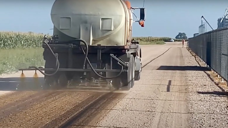 Truck spraying soybean oil over gravel path