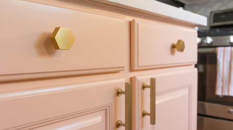 A closeup of a kitchen cabinet with shiny gold drawer pulls and door handles.