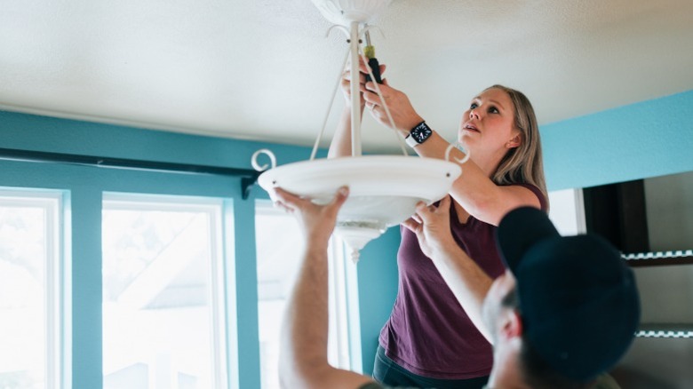 A man and a woman installing a light fixture in a ceiling.