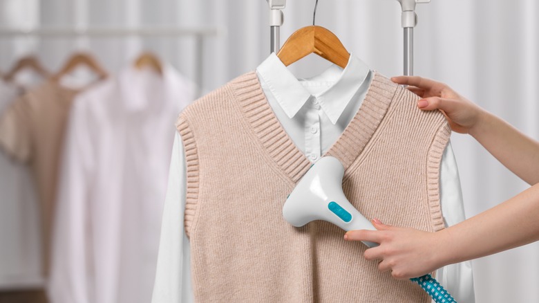 person using clothes steamer on sweater