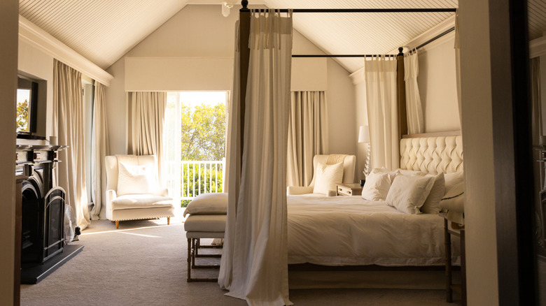 canopy bed with long drapes covering the box spring in a large bright bedroom