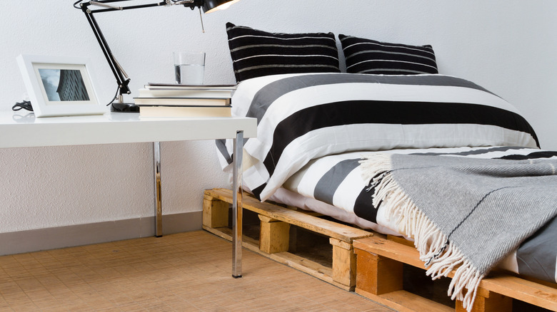 bed on wood pallet base in a bedroom next to a white desk