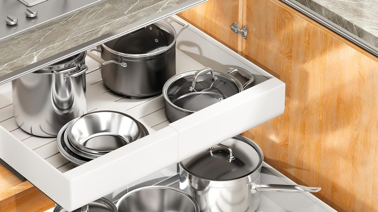 A pull-out drawer organizer with pots and pans in a cabinet