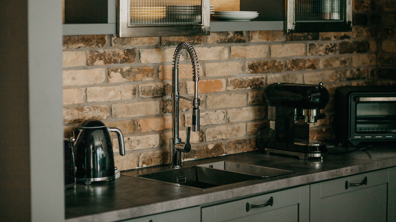 Kitchen with a brick wall with, black hardware, and dark sage cabinets
