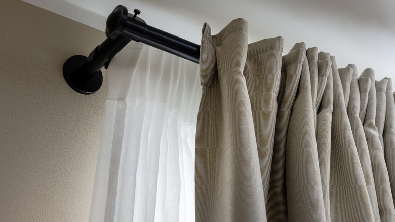 Layered transparent white and opaque beige curtains on a black rod