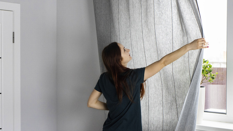 woman pulling closed her gray curtains in the living room