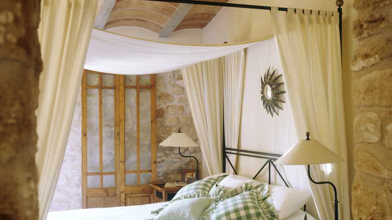 White curtains on a canopy bed in stone room