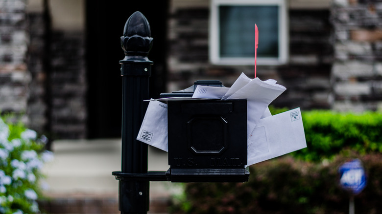 Black mailbox filled with unchecked mail in front of a home