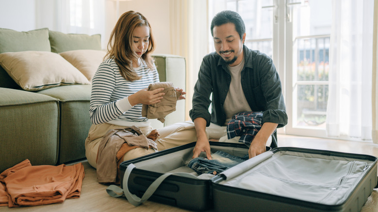 Asian couple packing a suitcase for vacation in their living room