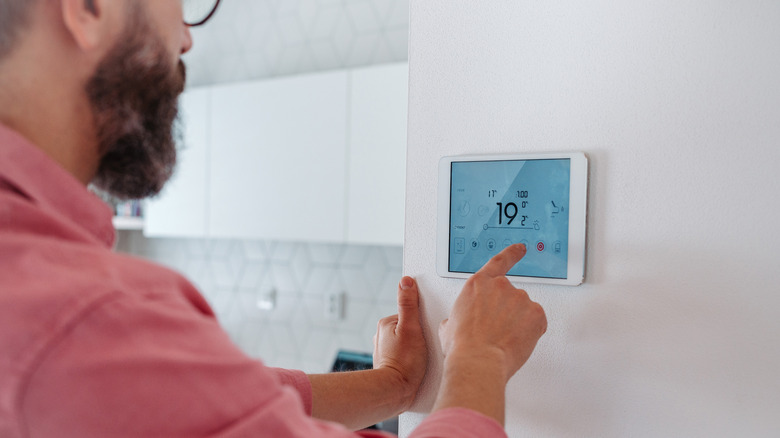 Man in red shirt setting the thermostat on a wall of his home