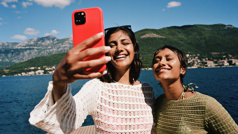 Two women together on a lakeside vacation destination taking a photo together on their smartphone