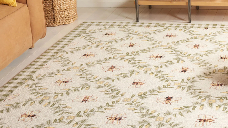 A wicker pouf sits on a diamond patterned floor rug featuring bees