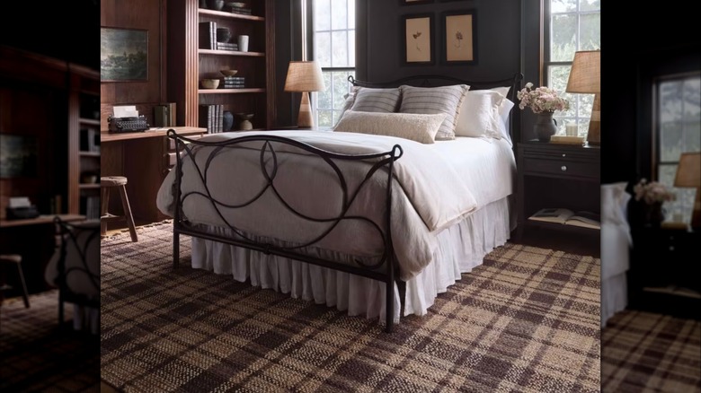 A plaid rug lays under a bed and side tables in a dark bedroom