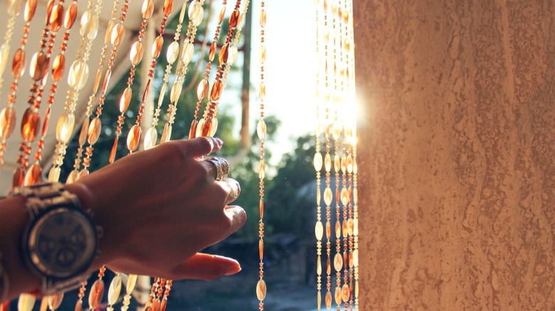 Hand pulling back beaded curtain on window