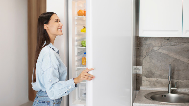 A woman opening a white refrigerator