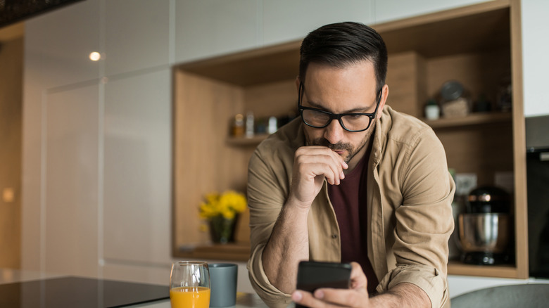 Man in kitchen researching on smartphone