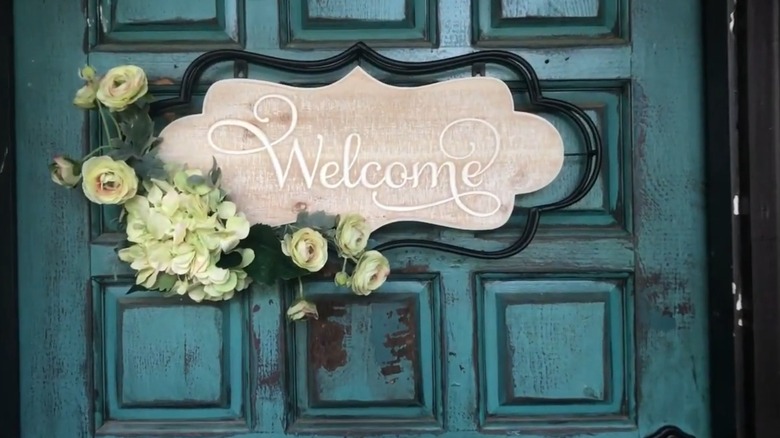 A welcome wall decor sign with flowers on a home's front door