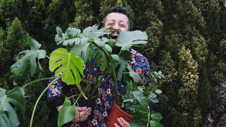 A man smiling while holding houseplants