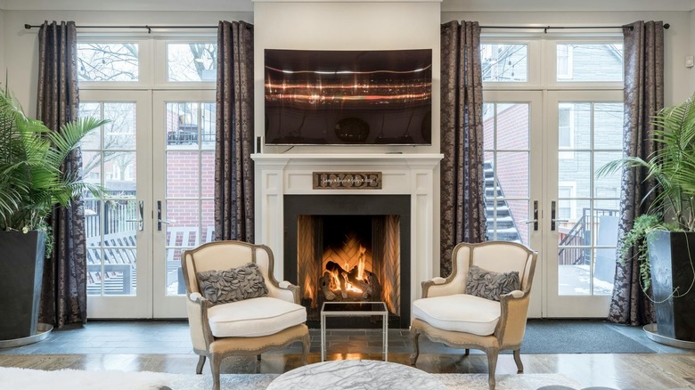 A living room with two large French doors with damask curtains and two statement chairs sitting in front of a fireplace.