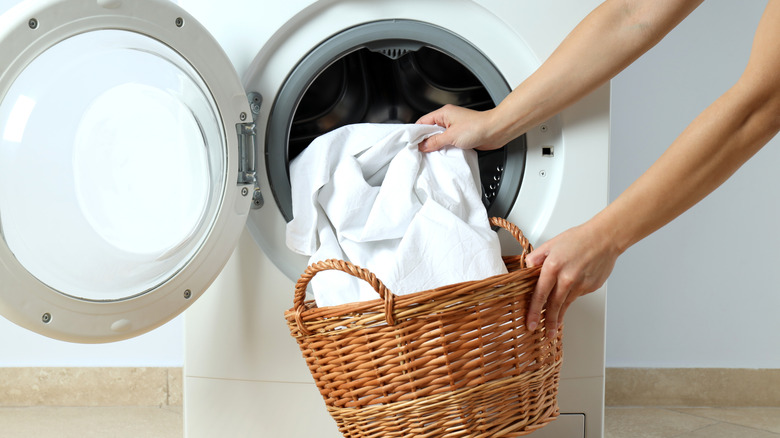 Hands placing white sheets in washing machine