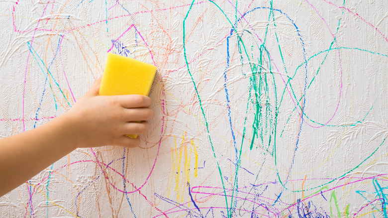 hands holding sponge up to a wall with crayon or marker