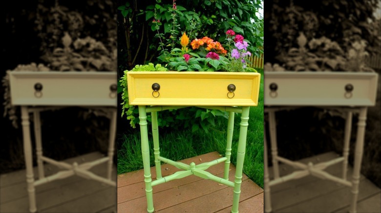 A pretty raised flower planter made from an old dresser drawer painted yellow with a timber stand painted in lime green