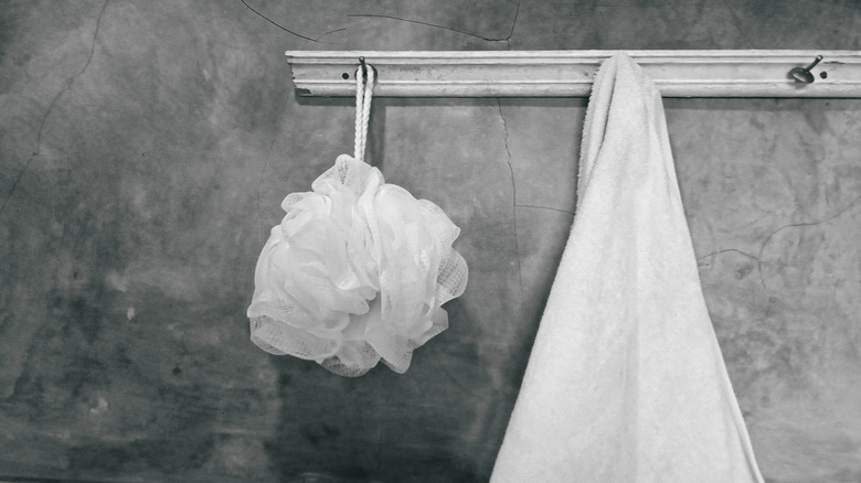 Towel and bath sponge hanging on hooks on bathroom wall