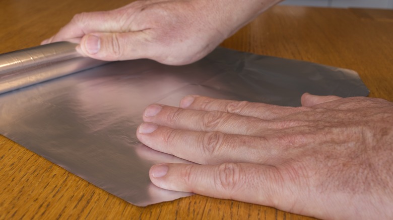 man's hands unrolling aluminum foil