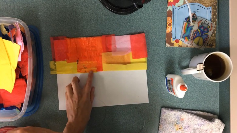 Person patting tissue paper onto a canvas to create a pretty sunset scene