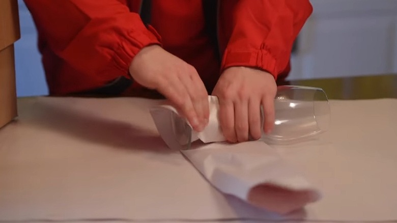 Person wrapping a wine glass in packing paper