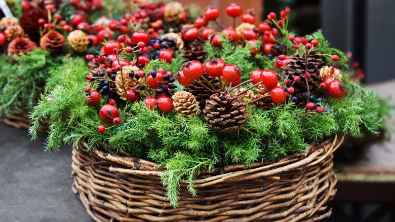 A wooden basket holds pine cones, evergreens, and red berries for a rustic winter holiday display.