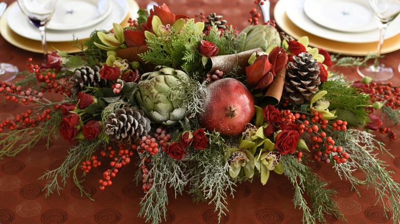 A creative centerpiece with pomegranates, artichokes, and sprays of evergreen is the focal point of a festive holiday meal.