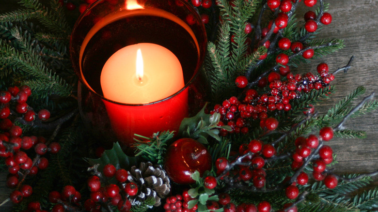 A red glass candle holder accents the red berries in a natural Yuletide display.