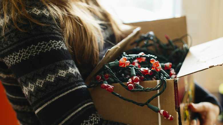 A woman carrying a box with holiday lights