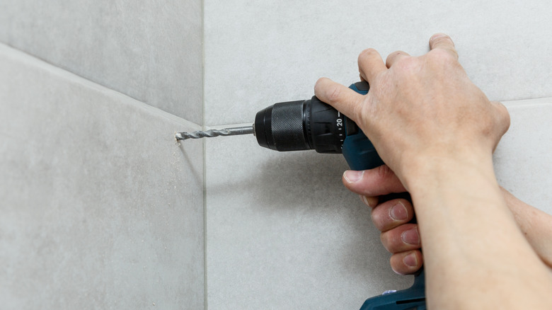 A man drilling into a tiled wall 