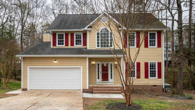 A two story subdivision house is painted in clashing colors of peach and dark red