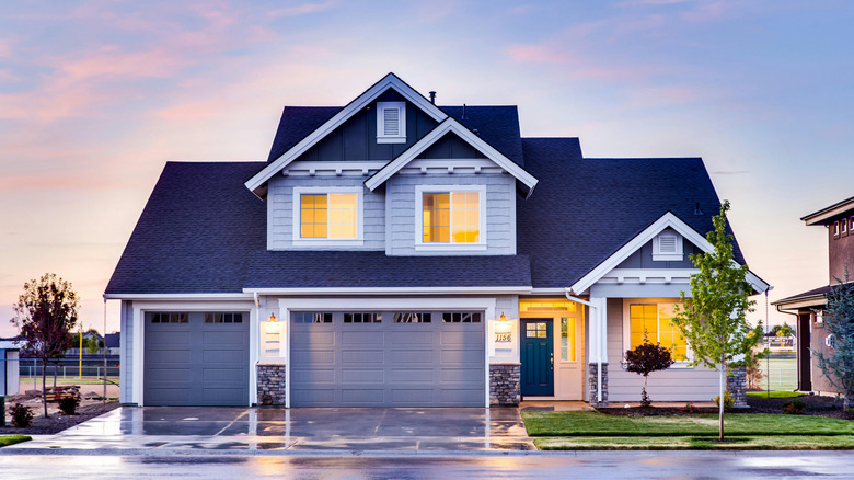 The sun sets behind a light gray house with a black roof