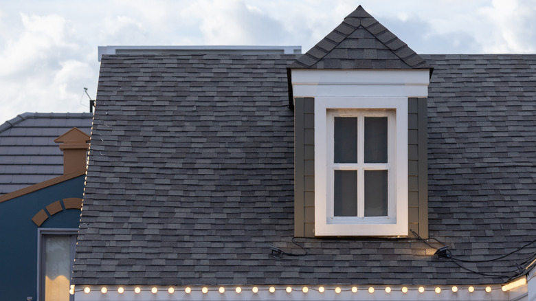 Lights are strung beneath a dormer window surrounded by a black shingled roof