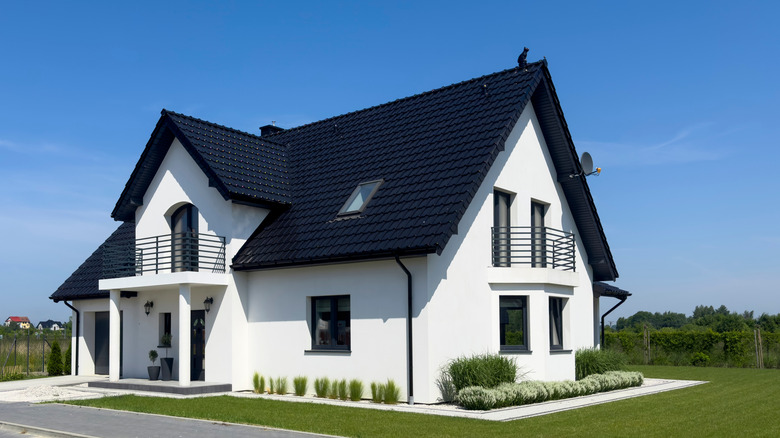 A modern black and white house is surrounded by green landscaping