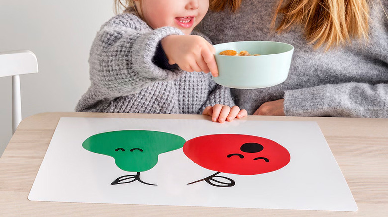 Child holding bowl above placemat