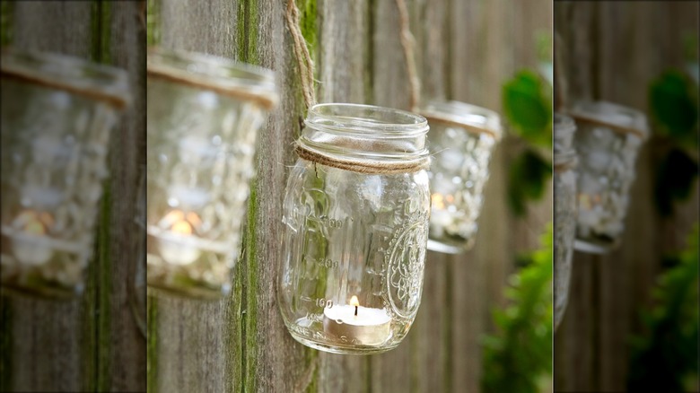 Mason jars with candles inside hanging on wood fence