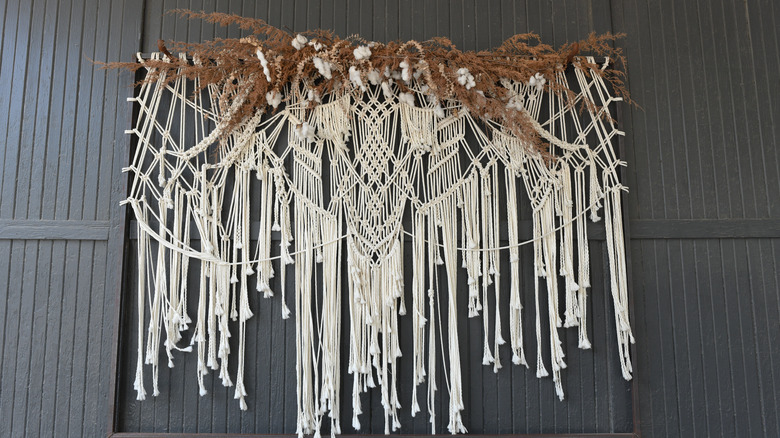 Macramé decoration with dried branches on dark gray wall